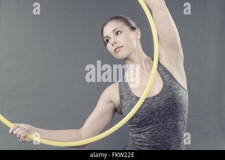 Giovane donna pratica con hula hoop e sfondo grigio Foto Stock