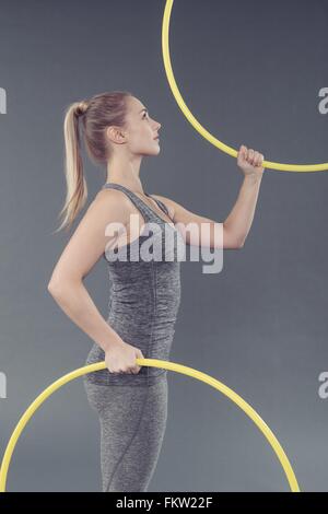 Giovane donna pratica con hula hoop e sfondo grigio Foto Stock