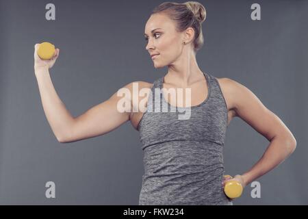 Giovane donna che lavora fuori con manubri e sfondo grigio Foto Stock