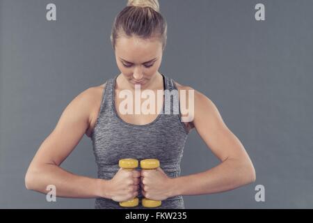 Giovane donna che lavora fuori con manubri e sfondo grigio Foto Stock