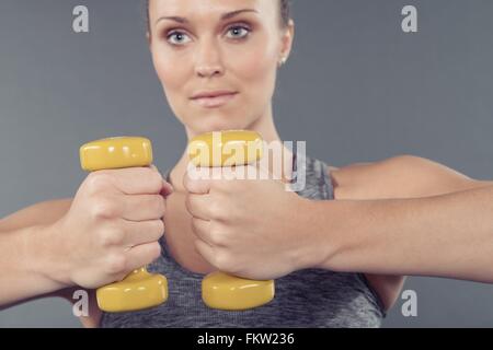 Giovane donna che lavora fuori con manubri e sfondo grigio Foto Stock