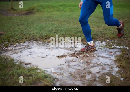 Gambe di runner in esecuzione attraverso la pozza di fango Foto Stock