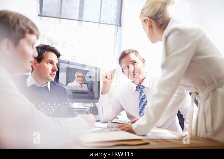 I colleghi in fice alla scrivania facendo chiamata video, avendo discussioni Foto Stock