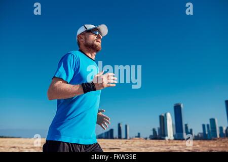 Basso angolo vista di metà uomo adulto in esecuzione da grattacieli, Dubai, Emirati Arabi Uniti Foto Stock