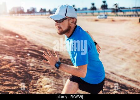 Metà uomo adulto che indossa cappello da baseball in esecuzione fino dune di sabbia, Dubai, Emirati Arabi Uniti Foto Stock