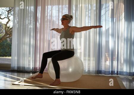 Donna matura in equilibrio su palla ginnica davanti le porte del patio Foto Stock