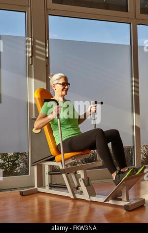 Donna matura facendo sedere esercizio in palestra macchina ginnica Foto Stock