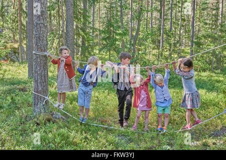 I ragazzi e le ragazze che indossano abiti retro equilibratura su funi in foresta Foto Stock