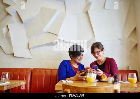 Due femmina adulta amici leggendo il testo dello smartphone in ristorante Foto Stock