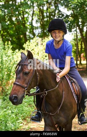 Ragazza sul cavallo che indossa riding hat guardando sorridente della fotocamera Foto Stock