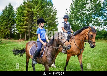 Donna matura e una ragazza a cavallo indossando cappelli a Cavallo sorridente Foto Stock