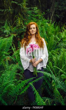 Giovane donna holding mazzo di gerbere rosa fra la foresta di felci Foto Stock