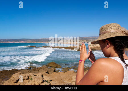 Giovani 20 anno vecchia donna sulla spiaggia in 'Tamraght' - Marocco. Scatto di una foto sul suo telefono cellulare Foto Stock