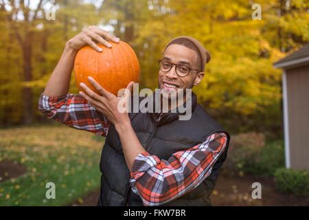 Ritratto di metà uomo adulto che trasportano la zucca sulla spalla in autunno giardino Foto Stock