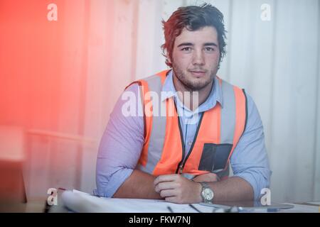 Ritratto di giovane maschio lavoratore edile seduto alla scrivania in cabina portatile Foto Stock