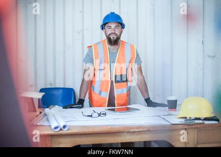 Ritratto di giovane maschio lavoratore edile permanente al desk in cabina portatile Foto Stock