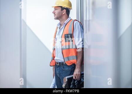 Costruzione foreman guardando fuori dalla porta della cabina portatile sul sito in costruzione Foto Stock