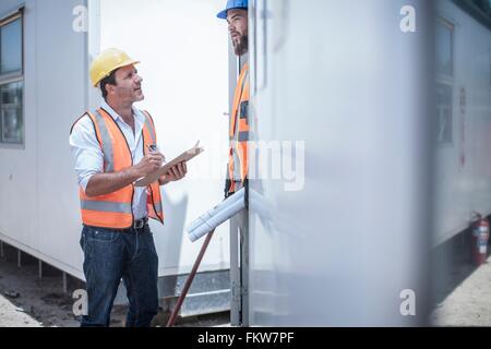 Operaio edile parlando a caposquadra dalla porta della cabina di costruzione Foto Stock