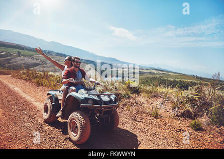 Una giovane coppia in un'avventura fuori strada. Uomo alla guida di moto quad con la ragazza seduta dietro e godendo la corsa in natura. Foto Stock