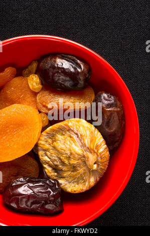 Varie la frutta secca nella piastra di colore rosso su sfondo nero Foto Stock