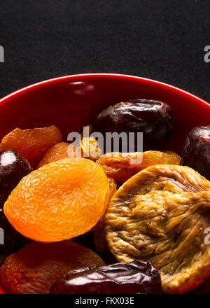Varie la frutta secca nella piastra di colore rosso su sfondo nero Foto Stock