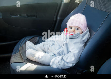 Il neonato in auto seduto sul sedile anteriore vestita per l'inverno onesie Foto Stock