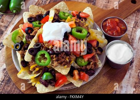 Messicano nacho chips e rabboccato con la carne di suolo, jalapenos, pomodori, fagioli e formaggio fuso con panna acida e salsa su un di legno Foto Stock