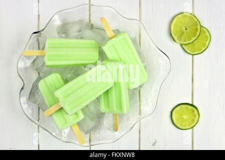 Frozen yogurt lime popsicles in un pieno di ghiaccio ciotola contro un bianco sullo sfondo di legno Foto Stock