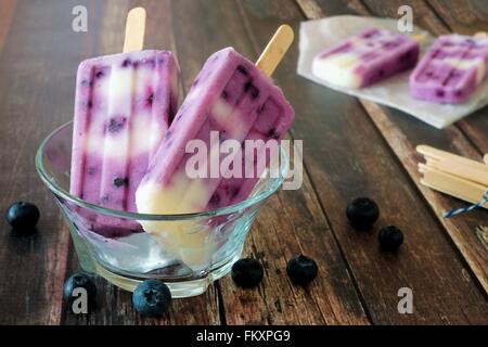 In casa mirtillo vaniglia popsicles in una ciotola ciotola trasparente contro un rustico sfondo legno Foto Stock