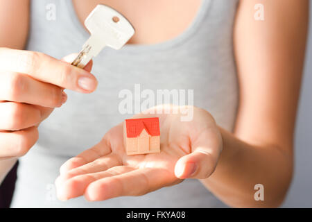 Close-up di donna di mani tenendo un piccolo modello di casa e un tasto suggerendo casa acquisto o noleggio Foto Stock