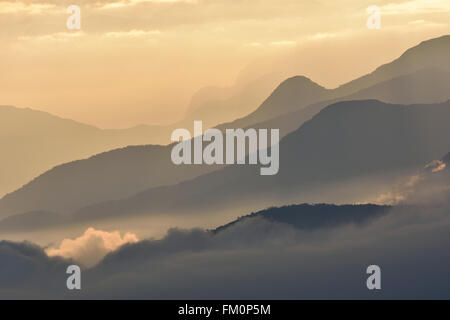 Misty creste montane all'alba con soffici nuvole immerso nelle valli. Foto Stock