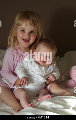 Baby sorella e big sister seduta su di un letto di ridere e giocare insieme Foto Stock
