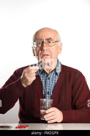 Il vecchio uomo senior prende pillole con acqua in una tazza di plastica Foto Stock