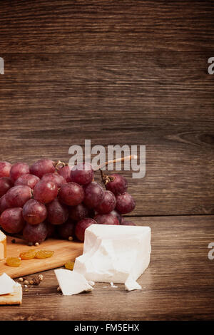 Formaggio bianco, dadi e uva rossa su sfondo di legno in tonificante vintage. Stile di vita sano Foto Stock