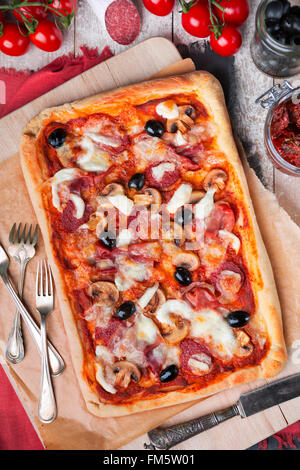 In casa rettangolare di salsiccia per pizza pizza su un tavolo rustico con ingredienti. Fotografato direttamente dall'alto. Foto Stock