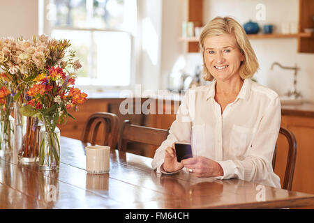 Senior donna utilizzando un telefono intelligente al tavolo di legno Foto Stock