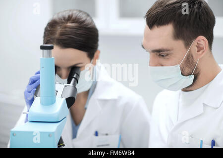 Gli scienziati nelle maschere guardando al microscopio in corrispondenza di lab Foto Stock