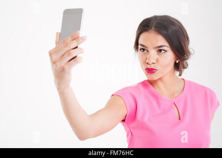 Carino bella giovane donna rendendo faccia d'anatra e tenendo selfie utilizza lo smartphone su sfondo bianco Foto Stock