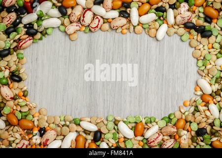 Misto di legumi secchi e cereali disposti intorno al grigio Sfondo di legno. Spazio di copia in medio Foto Stock