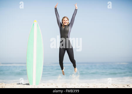 Excited donna muta jumping accanto alla sua tavola da surf Foto Stock