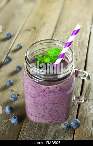 Frullato di mirtilli con menta in mason jar con paglia contro uno sfondo di legno Foto Stock