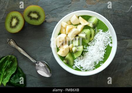 Frullato verde ciotola con spinaci, Banane, kiwi e cocco su un sfondo di ardesia Foto Stock