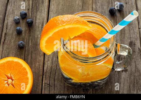 Detox acqua con arance e mirtilli in un mason jar con la paglia. Vista verso il basso su legno. Foto Stock