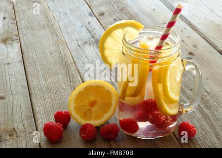 Vitamina Acqua con limone e lamponi in un vaso con paglia contro uno sfondo di legno Foto Stock