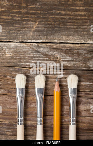 Tre pennelli e una matita su uno sfondo di legno Foto Stock