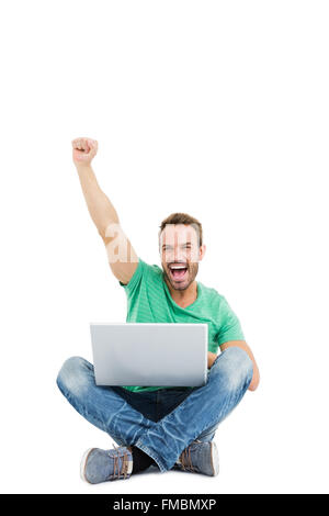 Felice giovane uomo che alza il pugno durante l'utilizzo di laptop Foto Stock