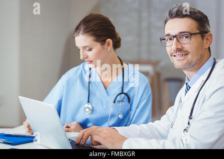 Ritratto di sorridente medico maschile seduto alla scrivania Foto Stock
