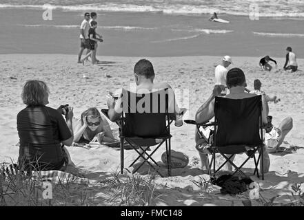 Beachgoers, prendere il sole e reclinabili in sedie, lettura, rilassante sulla Gold Coast di Queensland, Australia Foto Stock