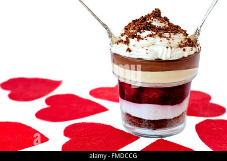 Layered dessert con biscotti sbriciolati sulla parte superiore, due cucchiai di argento a forma di cuore rosso tovaglioli isolato su bianco Foto Stock