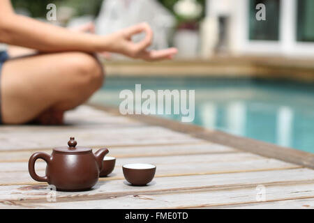 Donna meditando dalla piscina con tè pentola Foto Stock